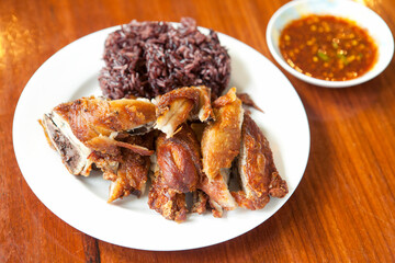 Sticky rice with crispy fried chicken served on a white plate, presenting a traditional Thai street food popular in Southeast Asia.
