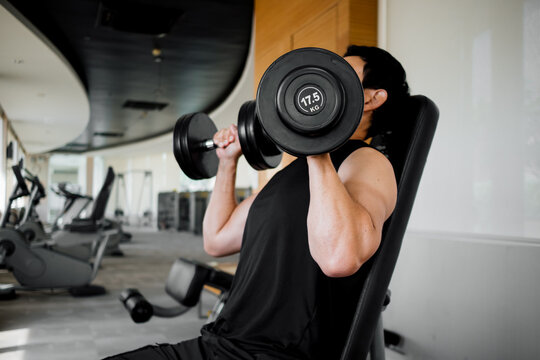 Asian man lifting dumbbells on bench in spacious gym