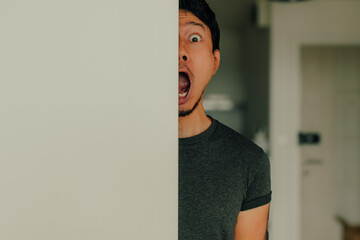 Thai man peeking from door with wide eyes and humorous surprised facial expression