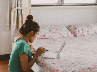 Thai woman sitting on bed using tablet and smartphone during daytime inside cozy bedroom