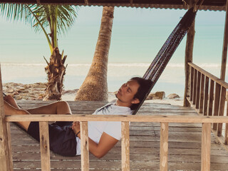 Chilling beach vibe of man sleeping on hammock in the hut by the beach.