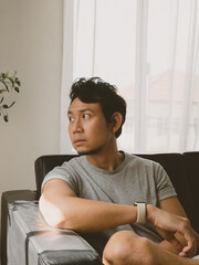 Thai man sitting on sofa and looking away in a calm and quiet modern interior