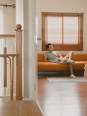 Asian man relaxing on orange sofa in vintage living room during daytime