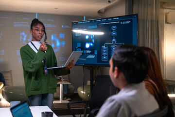 Programmer in office presents code on laptop to developer team while explaining software development concepts with digital flowchart on large screen during collaborative meeting