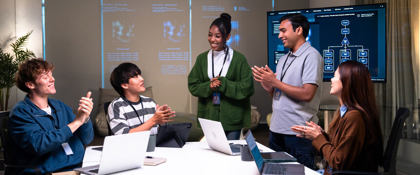 Programmer and developer team in office claps and smiles while discussing code and software development on laptops and digital screens creating positive work environment