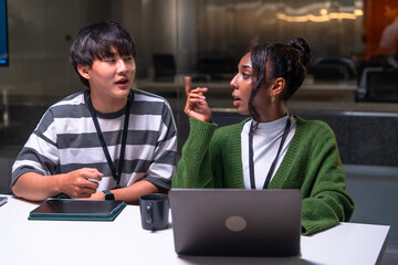 Two programmer developers discuss code in office environment with laptop and tablet on table showing focused collaboration and teamwork in modern workspace