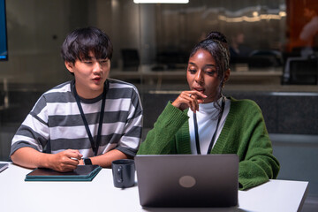 Two programmer developers working together in office environment focused on code development using laptop and tablet while discussing ideas and solving problems collaboratively