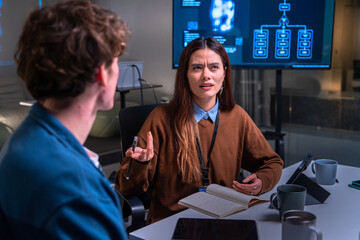 Programmer and developer discuss code in office setting with digital screen showing flowchart while woman expresses confusion during meeting