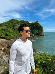 Asian man enjoying seaside walk in white long-sleeve shirt