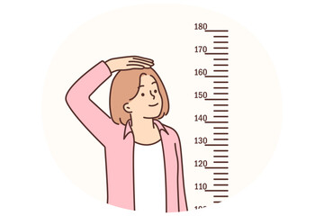 Teenage girl measures height standing near marks on wall, wanting to become tall