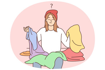 Embarrassed hipster woman cant choose what to wear holds in hands colorful clothes for party