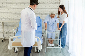 Senior woman receives physical support from caregiver and doctor while practicing walking with a...