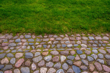 A cobblestone pavement next to the green grass on the lawn.