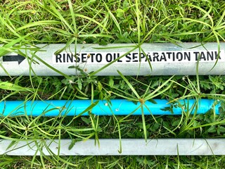 Industrial pipe labeled "Rinse to Oil Separation Tank" with directional arrow, surrounded by grass. Wastewater management system concept.