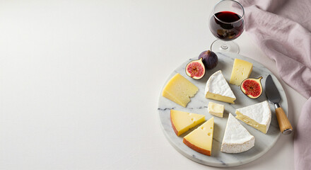 Gourmet marble cheese board with assorted brie, gouda and Swiss wedges, halved figs, wooden-handled cheese knife and red wine glass on light surface