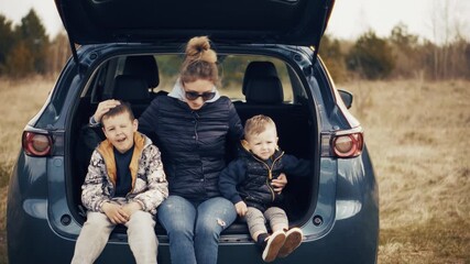 Happy mother with two sons sitting in open car trunk