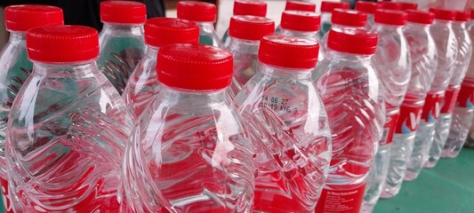 Rows of clear plastic water bottles with red caps are neatly arranged, reflecting light and creating a vibrant pattern