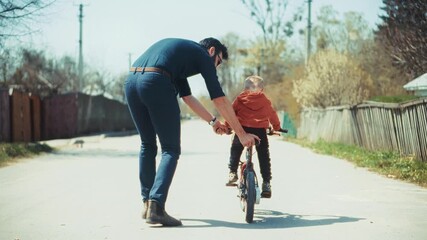 Father teaches his son to ride bicycle outdoors