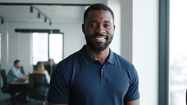 A smiling Black man in a blue polo shirt poses in a modern office setting