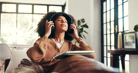 Headphones, woman and relax with tablet on sofa for audiobook, streaming podcast or online series. Cozy, african person and digital app in home for listening to sound playlist, music or weekend break