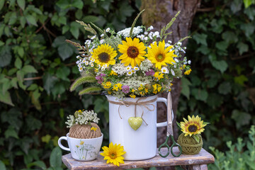 Blumenstrauß mit Sonnenblumen, einjährigem Berufkraut, Wilder Möhre, Hornklee und Gräsern im Emaille-Krug im Garten