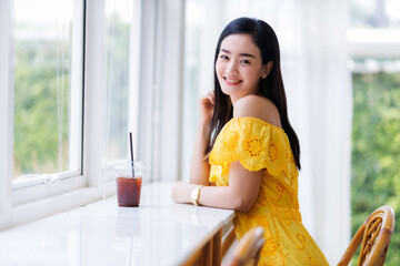 Portrait of beautiful happy Smiling asian woman relaxing sitting in yellow dress at cafe interior...