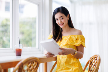 Portrait of beautiful happy Smiling asian woman relaxing sitting in yellow dress at cafe interior...