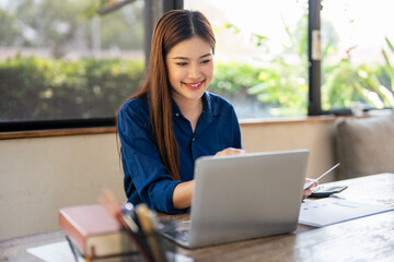 Young woman doing finance at home, holding paper document and looking at laptop.