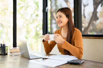 Remote work. woman enjoying coffee during work on laptop computer in home office, smiling and...