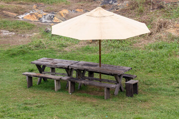 A wooden picnic table with a brown umbrella is sitting in a grassy field