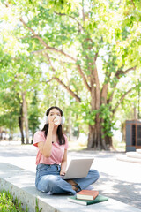 Young adult happy smiling asian student wearing headphones holding coffee using laptop sitting...