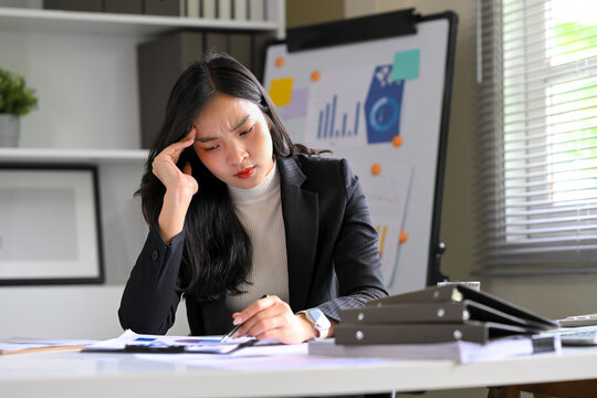 Stressed businesswoman reviewing financial documents at her desk