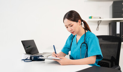 Serious female doctor using laptop and writing notes in medical report sitting at desk....