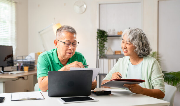 Senior old couple holding documents reading paper bills paying bank loan online, calculating pension fees, payments, taxes, planning family retirement money finances using laptop at home.