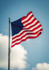 U.S. flag waves high on a flagpole against a clear blue sky with soft clouds