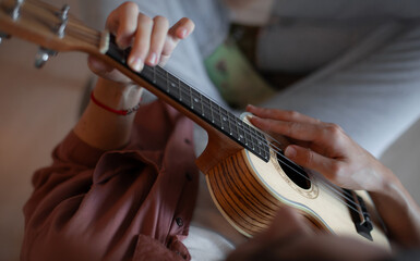 Close-up of a woman's hands playing a wooden ukulele, capturing finger placement on the frets and...