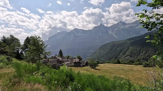 Traditional stone-roofed village near Varzo surrounded by alpine meadows, forests, and dramatic mountain peaks.