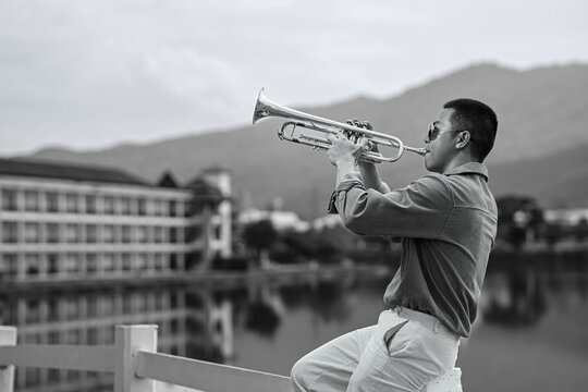 Stylish man performing trumpet on a lakeside balcony with scenic mountain backdrop
