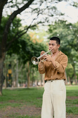 Young man playing the trumpet outdoors in a lush green park