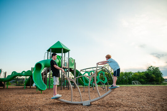 Brothers balancing on playground equipment during summer evening play
