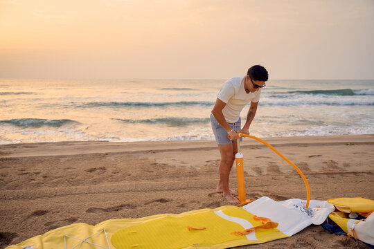 Sportsman inflating sup board at sunrise on sandy beach