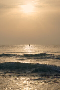 Lone paddler enjoys golden sunrise over calm ocean waves