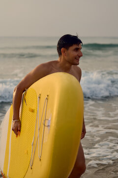 Surfer carrying paddle board on the beach at sunrise