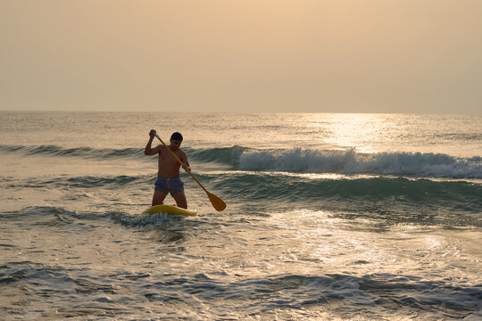 Man paddle boarding in the ocean at sunset, riding waves