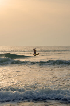 Man paddle boarding in ocean at sunset, enjoying surfing