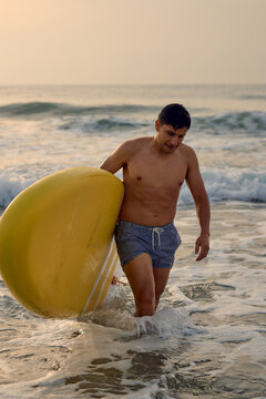 Man carrying surfboard at sunrise beach