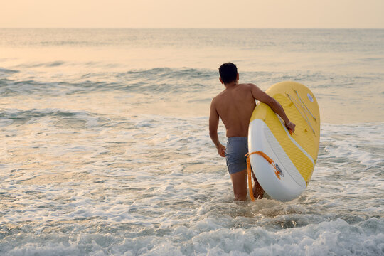 Surfer carrying paddle board into ocean at sunset