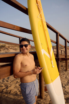 Smiling man relaxing with surfboard on sandy beach