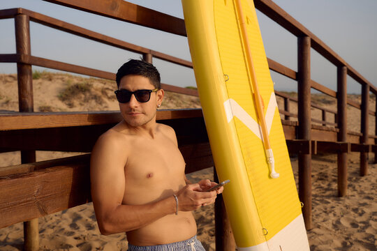 Surfer using smartphone near paddle board on beach
