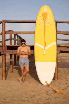 Man relaxing on beach with paddleboard and smartphone